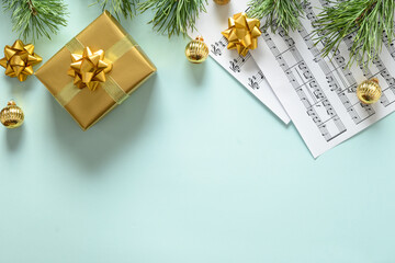 Music sheets for Christmas Carols and sings decorated golden gift and balls on blue background. View from above. Space for text.