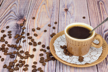 A coffee mug filled with black coffee sits on a saucer. Coffee beans are scattered around.