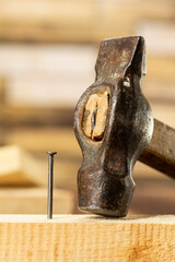 Old hammer and one single nail hammered into a wooden board, carpentry tools