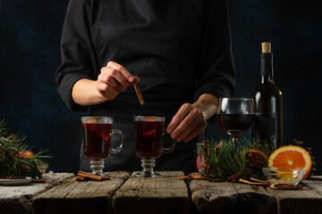 The chef serving glasses with mulled wine on rustic wooden table with festive composition background. Backstage of cooking hot drink with fragrant spices.