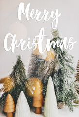 Merry Christmas text handwritten on little christmas trees in festive lights, miniature winter forest scene. Greeting card, modern seasons greetings. Happy holidays