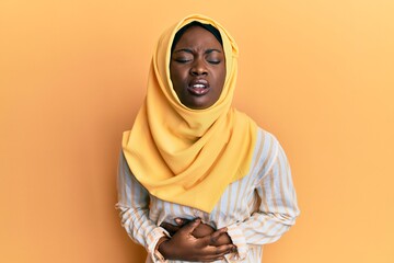 Beautiful african young woman wearing traditional islamic hijab scarf with hand on stomach because nausea, painful disease feeling unwell. ache concept.