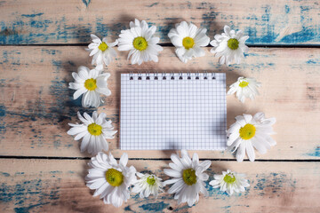 Blank notebook with white flower and bas ket of flower on vintage wooden table