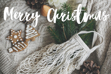 Merry Christmas text handwritten on cotton bag with green spruce branches, gingerbread cookies and...