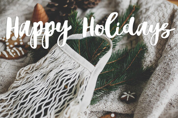 Happy holidays text handwritten on cotton bag with green spruce branches, gingerbread cookies and...