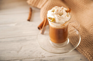 Pumpkin latte in a transparent mug close-up and copy space. Latte with cream, cinnamon, pumpkins, pumpkin seeds on a white plate. Latte and sweater.