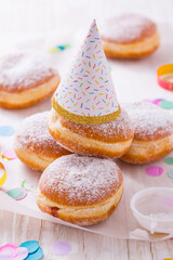 Traditional Berliner with party hat for carnival and party. German Krapfen or donuts with streamers and confetti.