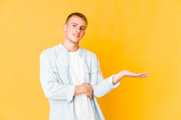 Young caucasian handsome man showing a copy space on a palm and holding another hand on waist.
