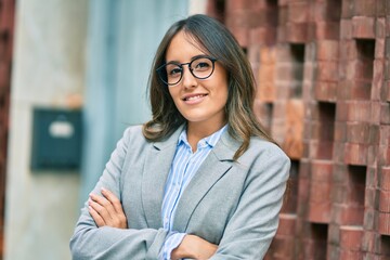 Fototapeta premium Young hispanic businesswoman with arms crossed smiling happy at the city