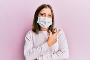 Young beautiful woman wearing medical mask smiling cheerful pointing with hand and finger up to the side