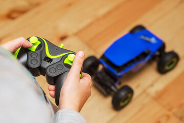 The boy is controling the blue toy car with a remote control. Child play with a toy car