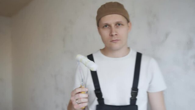 A man in overalls approaches the camera and paints the frame with a paint roller. 4K 50fps