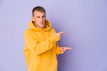 Young caucasian handsome man pointing with forefingers to a copy space, expressing excitement and desire.