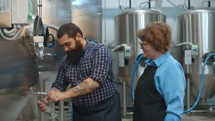 Brewery workers looking at freshly made beer in glass tube and tasting