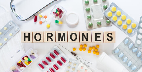 HORMONES. Word on wooden blocks on the table. Medical concept with pills, vitamins, stethoscope and syringe in the background.