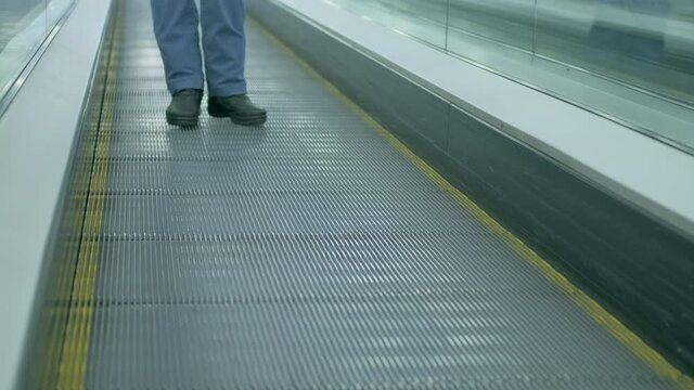 Iron, barrier-free escalator goes down. People in blue jeans and black shoes is standing on a rolling track