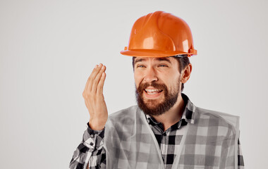 the architect gestures with his hands in an orange hard hat on a light background and a reflective vest