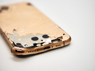 The back of modern gold smartphone with a broken glass and a damaged curved body close-up isolated...