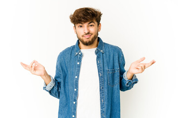 Young arab man on white background doubting and shrugging shoulders in questioning gesture.