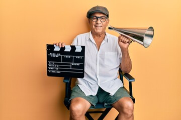 Handsome mature director man holding video film clapboard and louder smiling with a happy and cool...
