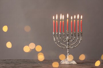 Silver menorah with burning candles on table against grey background and blurred festive lights, space for text. Hanukkah celebration