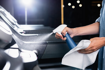 Naklejka premium partial view of charwoman holding rag while spraying cleanser on treadmill in gym on blurred foreground