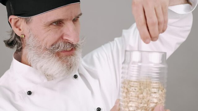 Cooking, healthy food. Professions and jobs. The man in chef's equipment standing with a pot and bootle of cereals on grey copy space.