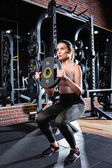 Fototapeta na wymiar athletic sportswoman in leggings doing sit ups with weight disk in gym
