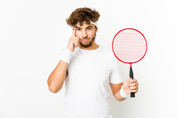 Young indian man playing badminton pointing temple with finger, thinking, focused on a task.