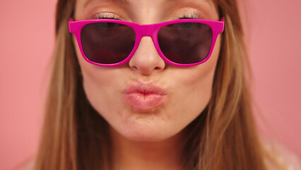 Young caucasian woman with pink sunglasses blowing her lips and sending kisses. High quality photo