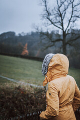 Rear view of an unrecognizable woman wearing a yellow winter coat with her fur hood on in nature looking at the view