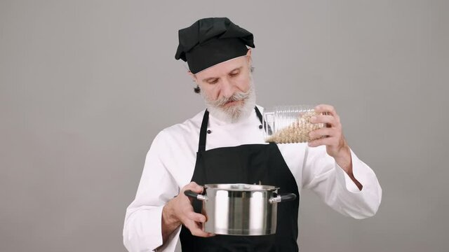 Cooking, healthy food. Professions and jobs. The man in chef's equipment standing with a pot and bootle of cereals on grey copy space.