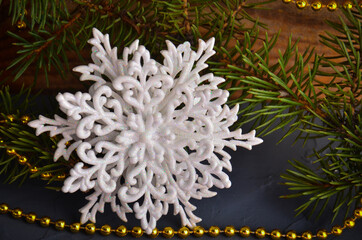 White snowflake with fir branches on a background of concrete and wood with a golden garland.