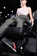 Naklejka na ściany i meble young sportswoman doing leg extension exercise on training machine on blurred background