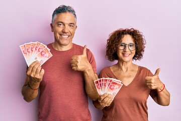 Beautiful middle age couple holding 20 israel shekels banknotes smiling happy and positive, thumb...