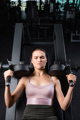 Fototapeta na wymiar top view of sportswoman with closed eyes training on arms extension machine in gym
