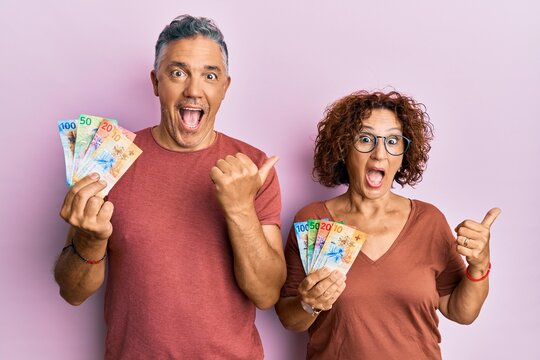 Beautiful middle age couple together holding swiss franc banknotes pointing thumb up to the side smiling happy with open mouth