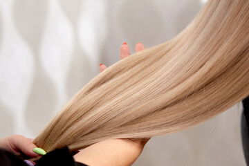 Beautiful white long hair in the hand of a female hairdresser. Professional hair care products. Hair coloring.
