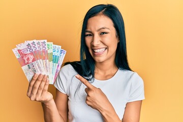 Beautiful hispanic woman holding hong kong dollars banknotes smiling happy pointing with hand and finger