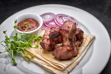 Fried shish kebab with lavash, sauce, microgreen and onion, on a white plate, on a gray background