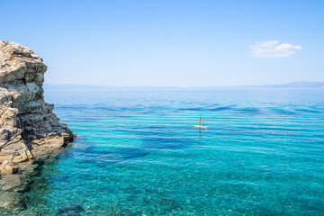 A single lonely girl on yellow paddle board or sup surf wearing red bikini paddling in the turquoise crystal clear water of mediterranean sea in Greece with single cloud  