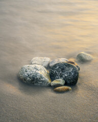 A bunch of round pebbles or sea stones of different colors on a sand beach of mediterranean sea surrounded by milky water long exposure 