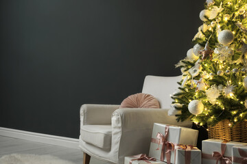 Beautifully decorated Christmas tree, gift boxes and armchair near black wall indoors, space for text