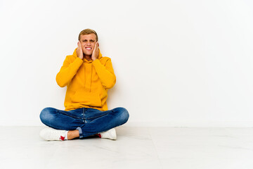 Young caucasian man sitting on the floor covering ears with hands.