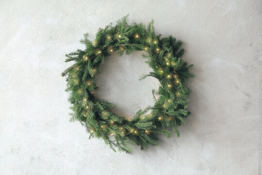Beautiful Christmas wreath with festive lights on light wall