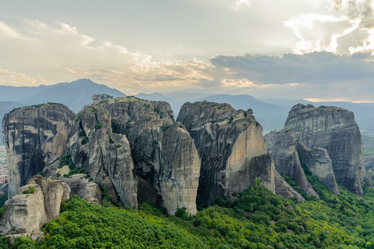 Meteora rock formation in Greece . Unique and enormous columns of rock rising high lit by rays of settin sun at the sunset and with dramatic clouds above. Amazing place © Kirill