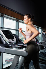 side view of sportswoman in leggings looking away while running on treadmill