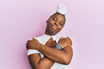 Young african woman wearing hair turban over pink background hugging oneself happy and positive, smiling confident. self love and self care