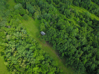 Fototapeta na wymiar Aerial drone view over a hilly forested landscape. An old wooded hut lays into the middle of the forest, in a green pasture, Carpathia, Romania.
