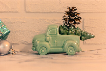 A toy car carries New Year's gifts, Christmas tree toys and a pine cone against a white brick wall. 